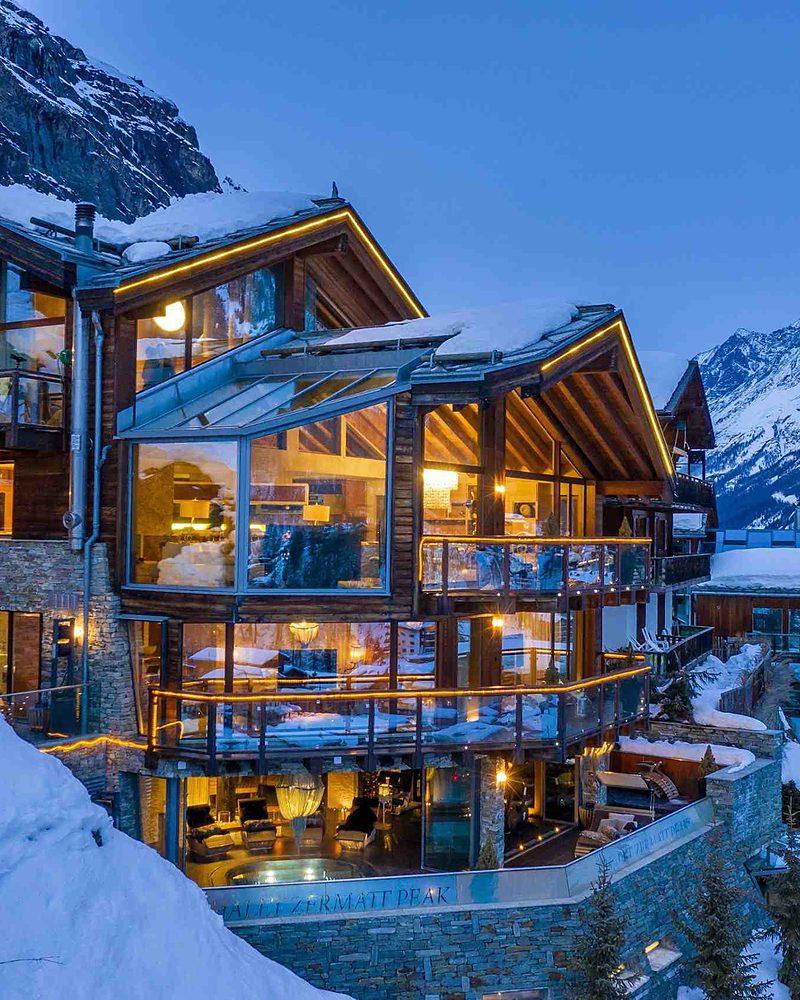 Chalé de luxo iluminado ao entardecer nos Alpes suíços, cercado por montanhas nevadas