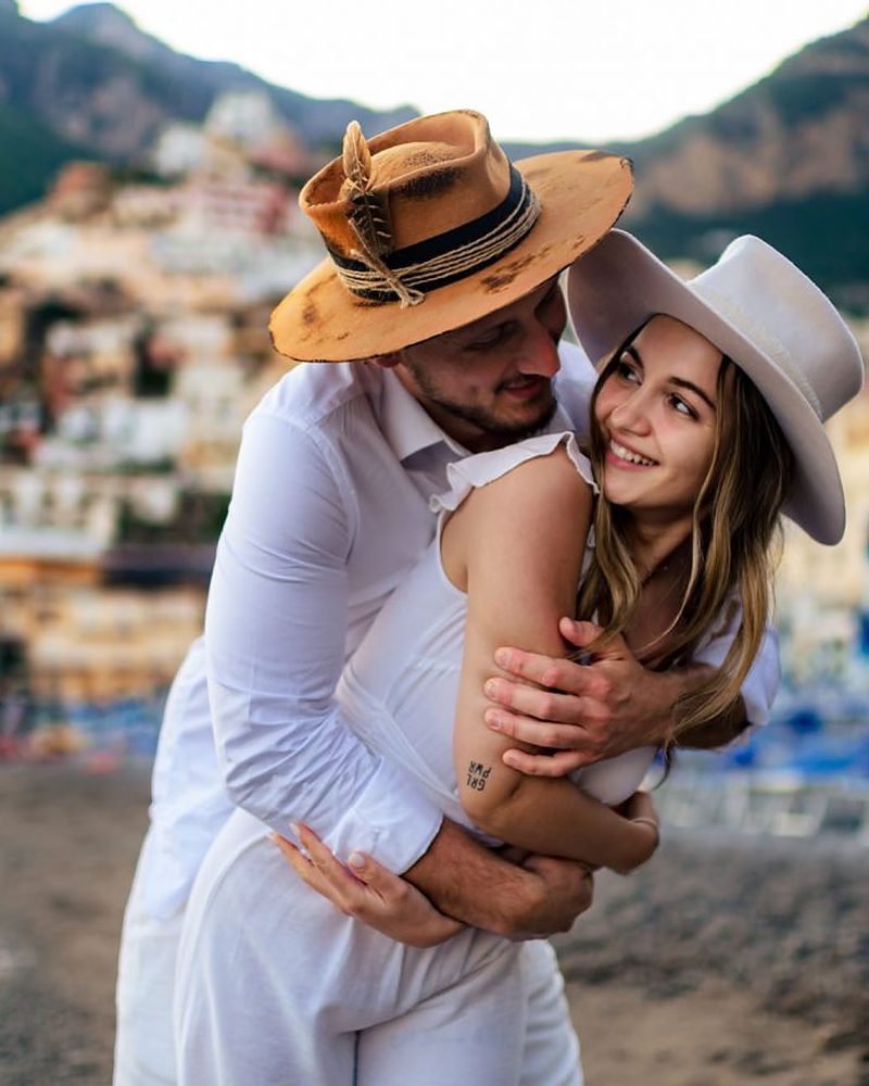 Casal abraçado na Costa Amalfitana, com o vilarejo de Positano ao fundo