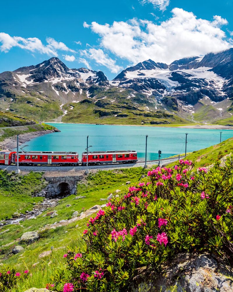 Trem panorâmico vermelho cruzando os Alpes entre lago e montanhas nevadas