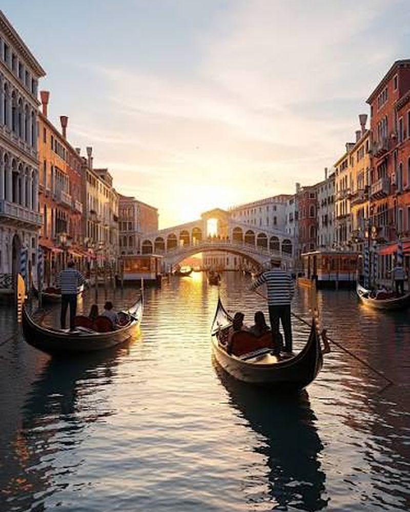 Gôndolas navegando os canais de Veneza ao entardecer, com a Ponte de Rialto ao fundo